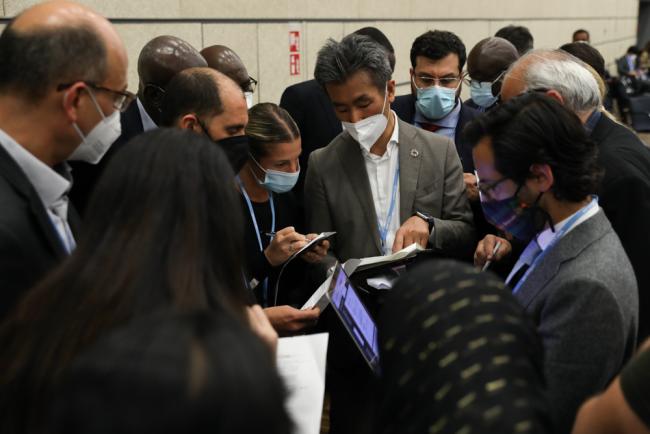 Delegates huddle during the informal consultations on the work program for Article 6.8